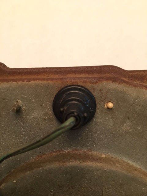 1968 Mercury Cougar - A close-up view of a wiring grommet on a rusty metal panel, showing a green wire passing through.