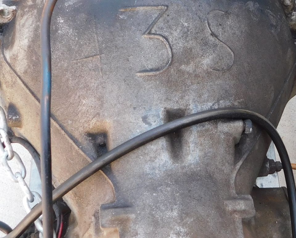 Close-up of a transmission casing with '3S' cast into it. A chain and hoses are visible