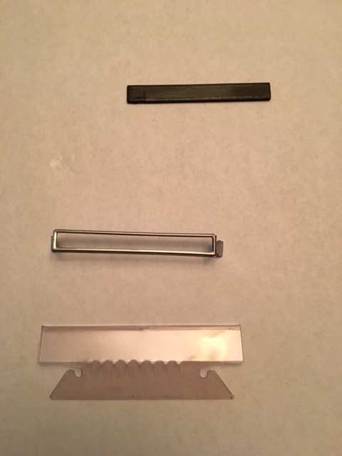 1968 Mercury Cougar - A close-up view of a razor blade with a serrated edge, a metal frame, and a dark rectangular object.