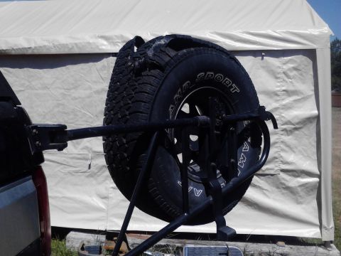 1995 Ford Bronco - A damaged spare tire is mounted on a rear carrier attached to a dark-colored SUV.