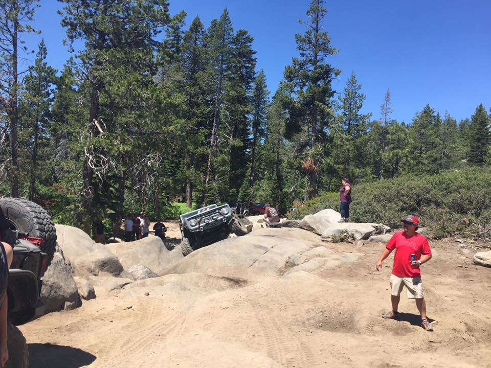 Off-road vehicle climbing over rocks with people watching