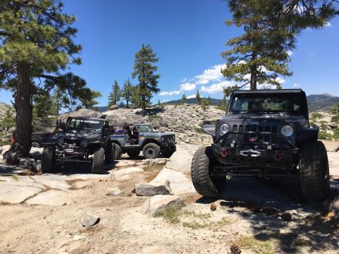 1979 Ford Bronco - Three off-road vehicles are parked on a rocky trail in a wooded area on a sunny day.