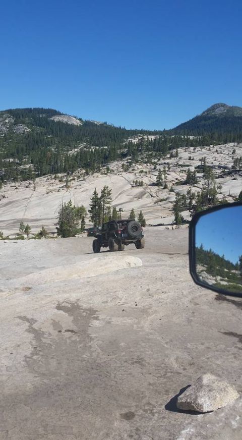 1979 Ford Bronco - An off-road vehicle navigates a rocky terrain under a clear blue sky, as seen reflected in a side mirror.