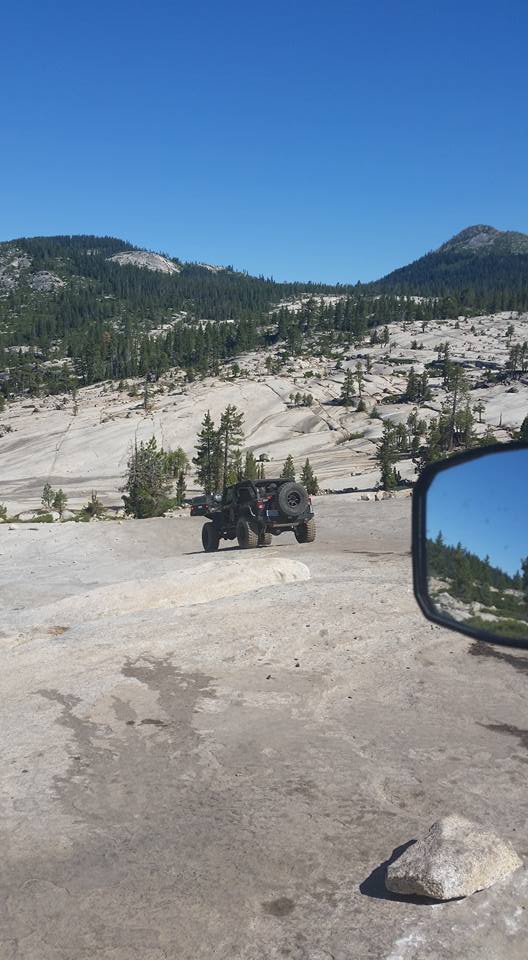 Off-road vehicle with spare tire on back, seen from side mirror in a rocky, mountainous landscape