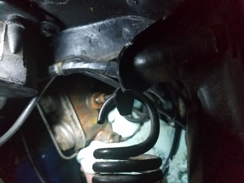Close-up of a car's suspension spring and metal bracket, with some wiring visible