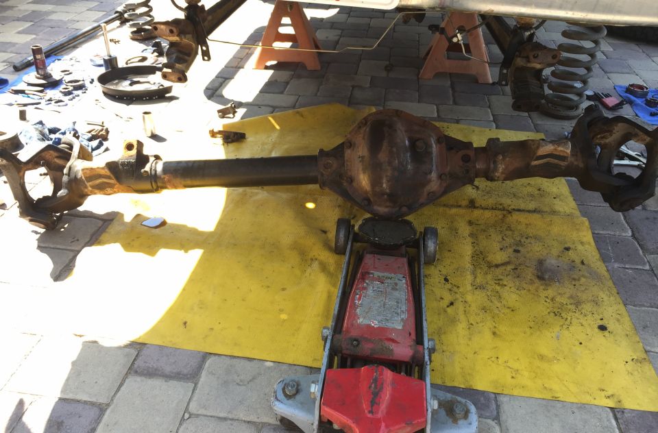 Rusty solid axle with differential resting on a red floor jack over a yellow tarp during teardown