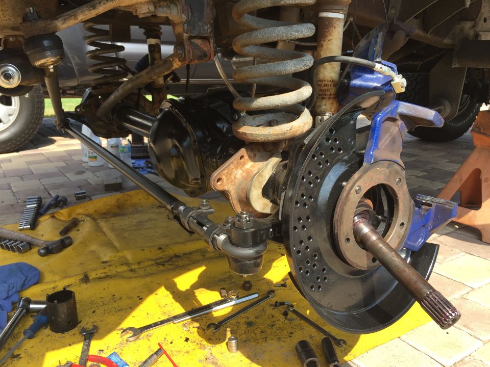 Close-up of vehicle's front axle, steering linkage, and suspension parts laid out on a yellow tarp with tools