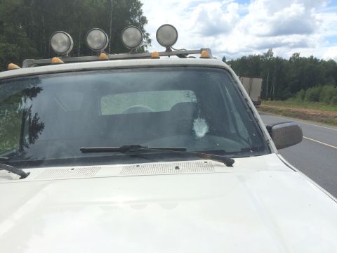 1993 Ford Bronco - White SUV with auxiliary lights on the roof is seen from the front, driving on a road with a truck in the background.