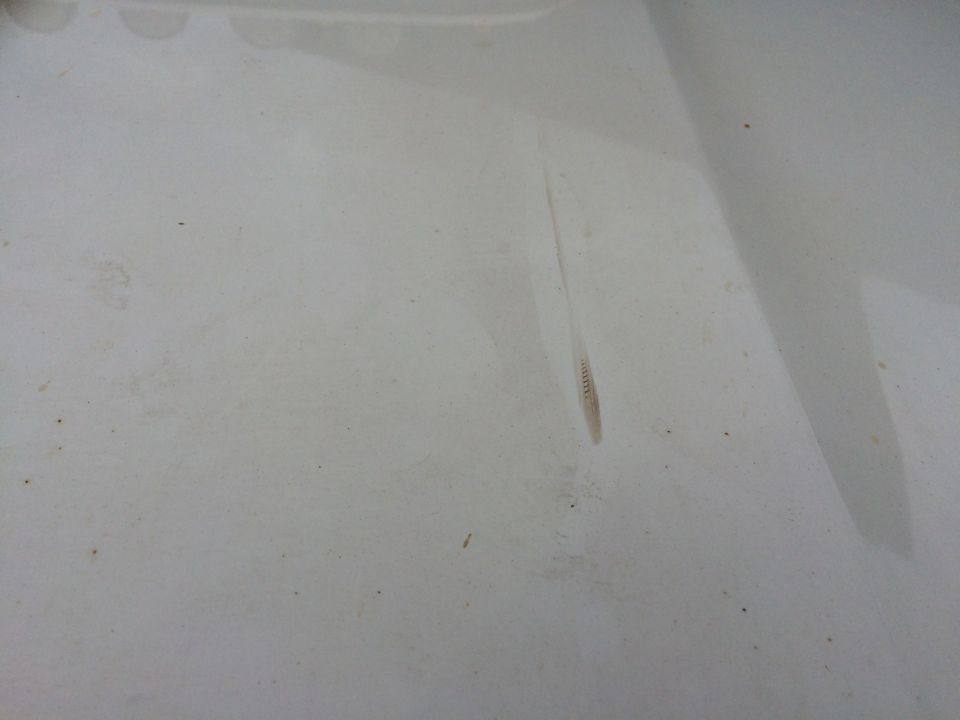 Close-up of a white car hood with a faint scratch and some dirt specks. Supermotors.net logo visible at bottom right