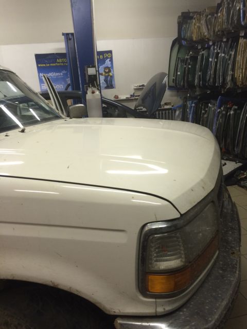 1993 Ford Bronco - A white pickup truck is parked in a garage with its hood up, next to another vehicle.