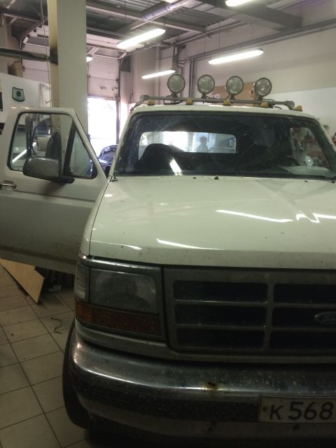 1993 Ford Bronco - White Ford F-Series truck with aftermarket lights on roof rack, seen from the front with the driver's door open.