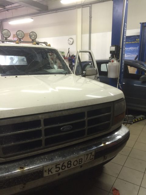 1993 Ford Bronco - A white 1993 Ford Bronco is parked in a garage, showing its front grille and cracked windshield.