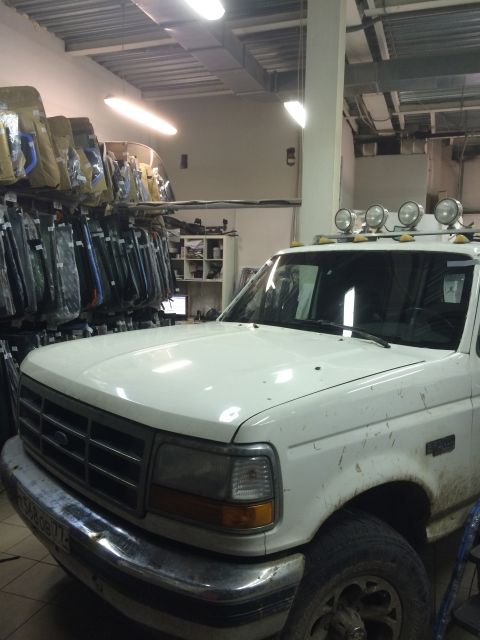 1993 Ford Bronco - White Ford truck with chrome bumper and roof lights, viewed from front-right, parked indoors.
