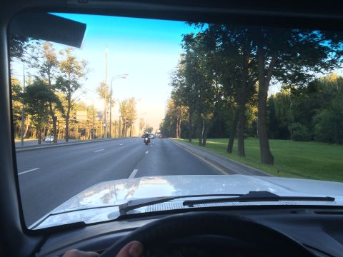 1993 Ford Bronco - View from inside a vehicle as it travels down a road lined with trees, with a motorcycle visible in the distance.