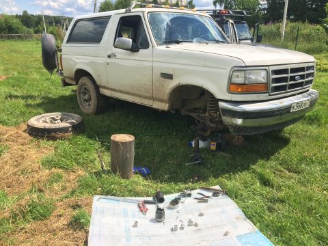 1993 Ford Bronco - A white Ford Bronco is undergoing maintenance outdoors, with its front wheel removed and parts scattered on a cloth.