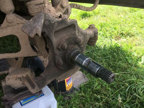 1993 Ford Bronco - Close-up view of a muddy vehicle's front wheel hub and axle assembly, supported by a jack.