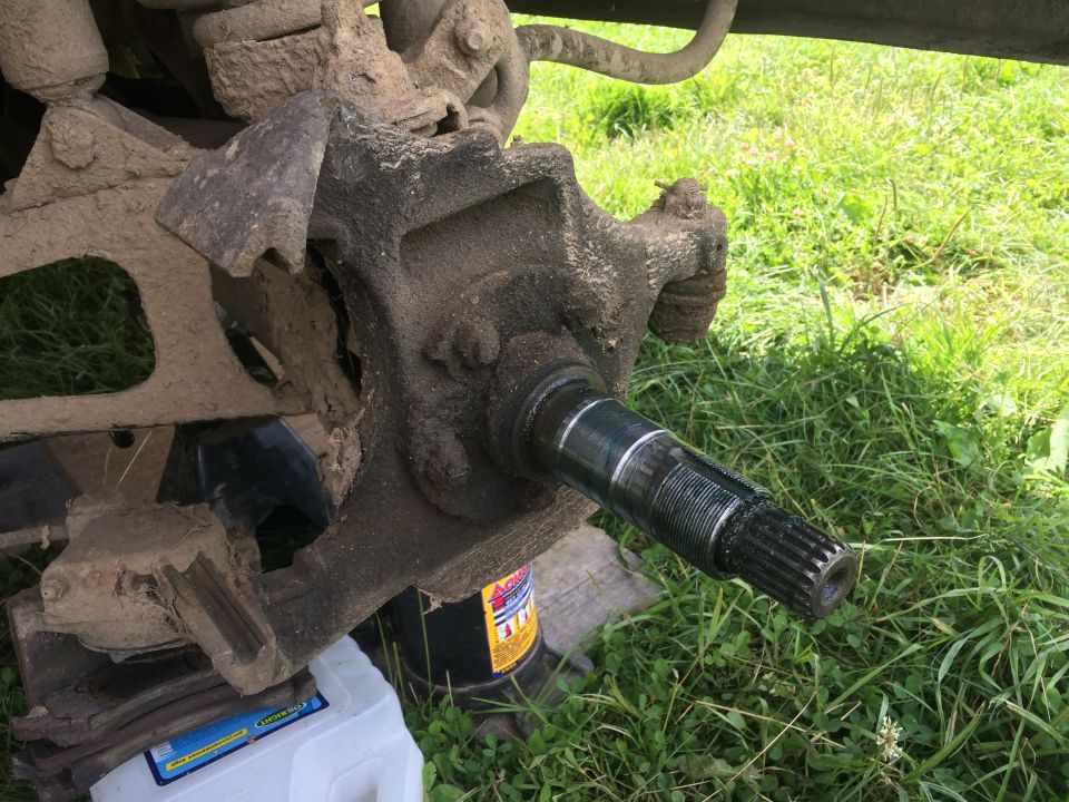 Vehicle's front wheel hub and axle assembly, heavily soiled with mud, with a jack visible underneath