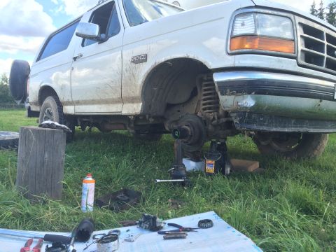 1993 Ford Bronco - The front wheel assembly of a white 1993 Ford Bronco is disassembled for repair outdoors.