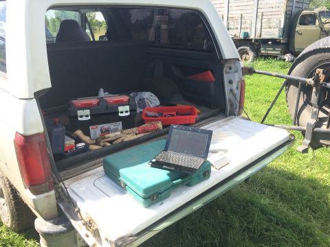 1993 Ford Bronco - Open tailgate of a white SUV reveals a collection of tools and a laptop, with another truck visible in the background.