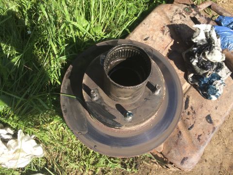 1993 Ford Bronco - A wheel hub and brake rotor assembly sits on the ground, surrounded by grass and a dirty shovel.