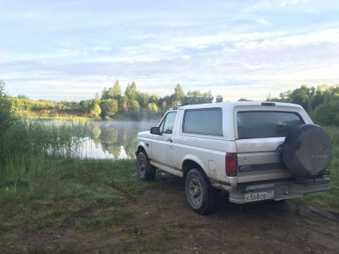 1993 Ford Bronco - A white Ford Bronco is parked on a dirt path next to a lake with morning mist.