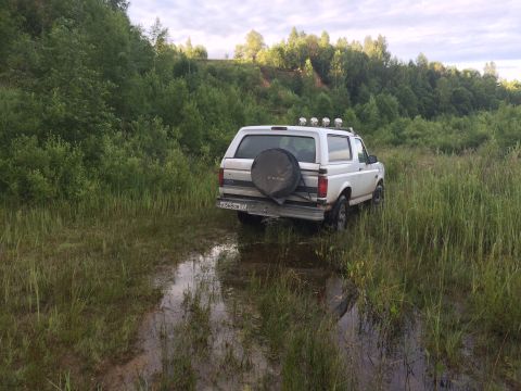 1993 Ford Bronco - White Ford Bronco with spare tire on rear, stuck in muddy field with trees in background.