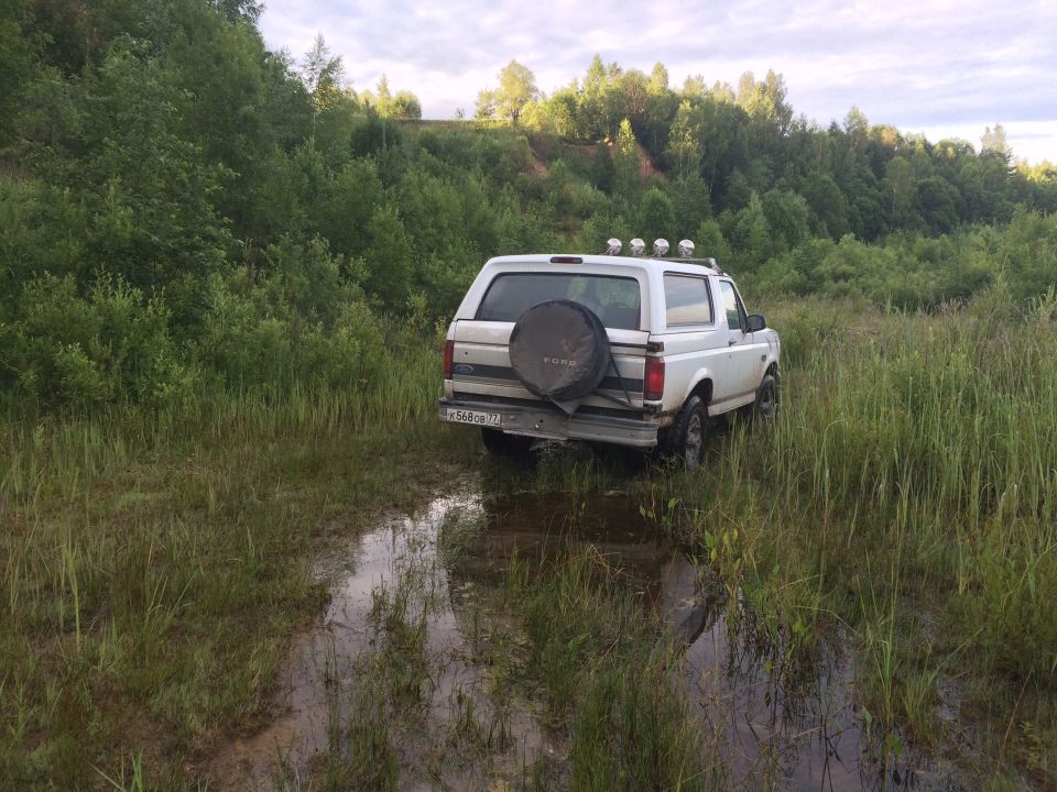 White Ford Bronco with spare tire on rear, stuck in muddy field