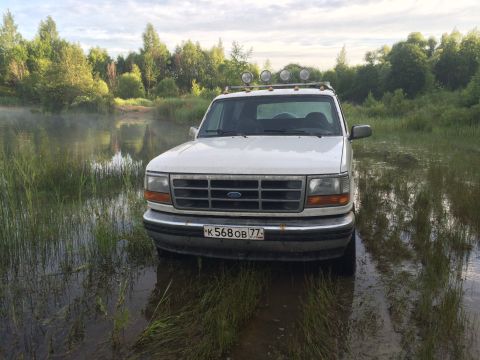 1993 Ford Bronco - A white Ford Bronco sits in a misty, grassy area near a body of water under a cloudy sky.