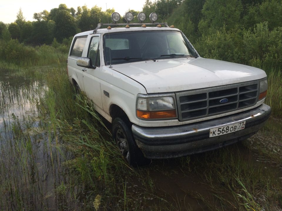 White 1992 Ford Bronco partially submerged in water and mud, front grille visible