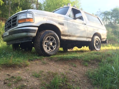 1993 Ford Bronco - A white Ford Bronco is parked on a dirt path with grass and trees in the background.