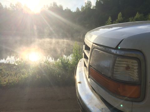 1993 Ford Bronco - A white Ford F-Series truck is parked by a misty lake as the sun rises, casting rays through the morning fog.