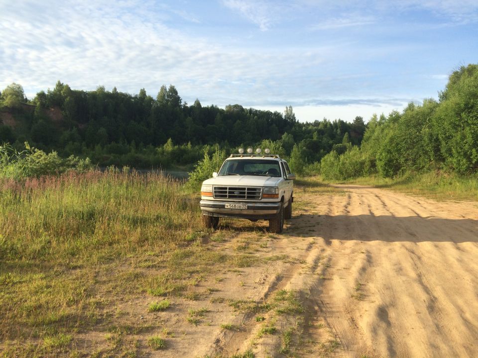 White 1993 Ford Bronco parked on a dirt road with trees in the background