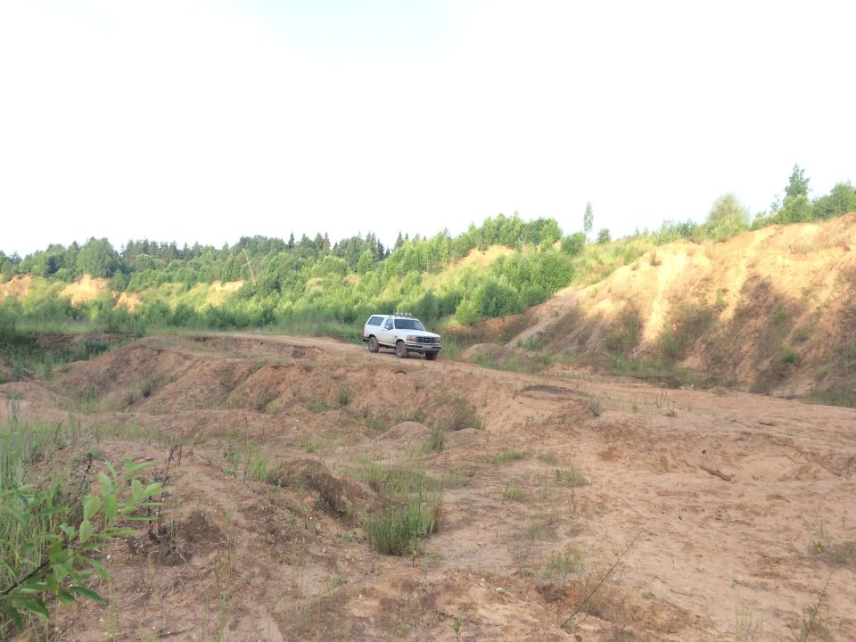 White 1992 Ford Bronco driving on a dirt road in a sandy, hilly area