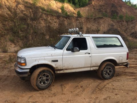 1993 Ford Bronco - White Ford Bronco with roof lights navigates a muddy off-road trail.