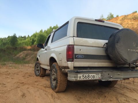 1993 Ford Bronco - Rear view of a white Ford Bronco on a dirt track with trees in the background.