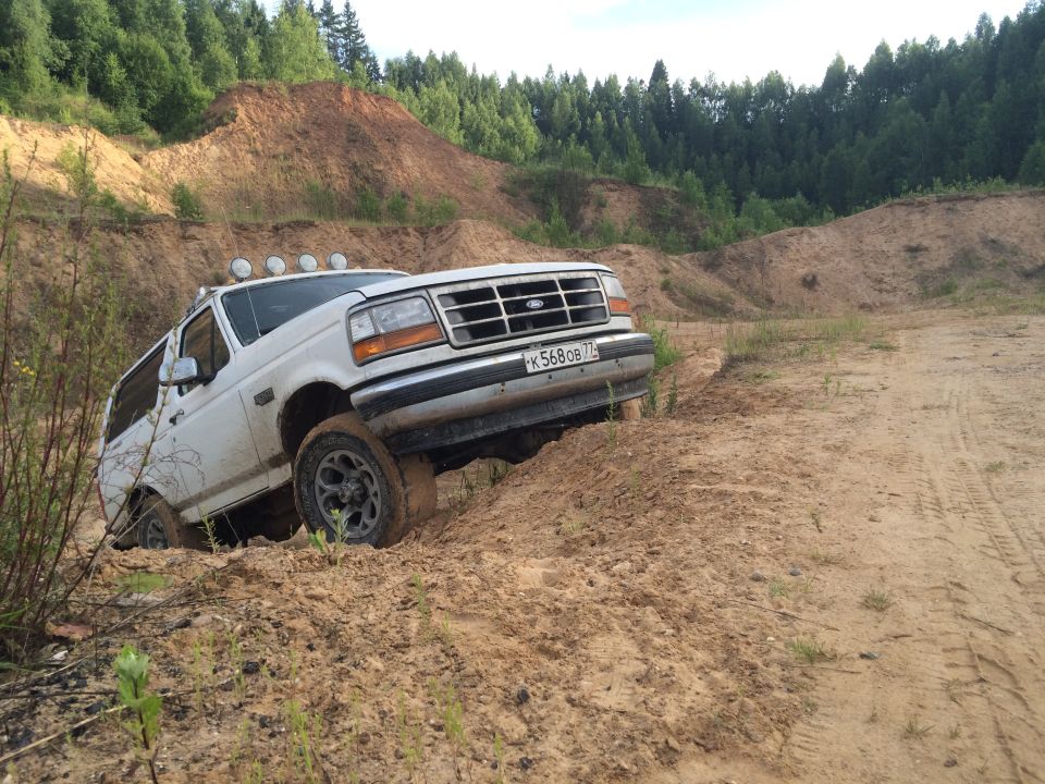 1993 Ford Bronco driving through sandy terrain with trees in background