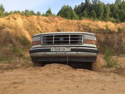 1993 Ford Bronco - A white Ford F-Series truck is stuck in a sandy, off-road environment with a prominent grille.