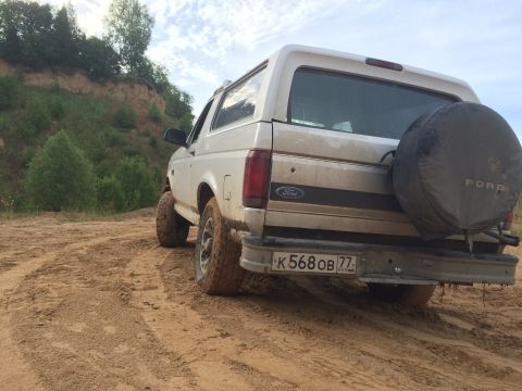 1993 Ford Bronco - A white 1993 Ford Bronco is seen from the rear on a dirt road, equipped with a spare tire mounted on the back.