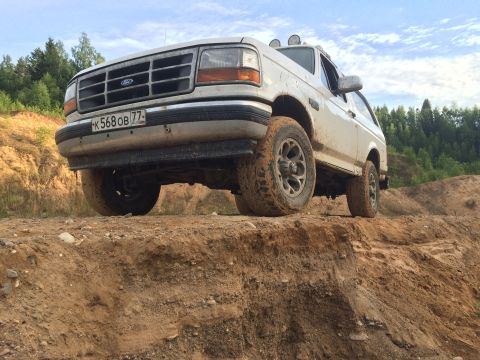 1993 Ford Bronco - This 1993 Ford Bronco is shown off-roading on a dirt trail with a wooded area behind it.