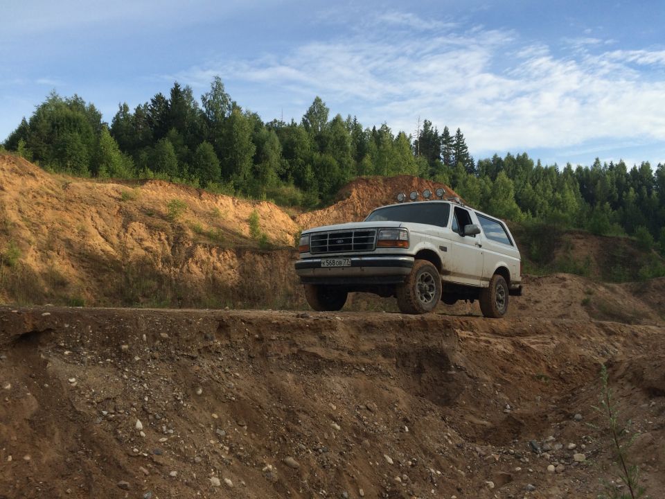 White Ford Bronco on a dirt road with trees in the background