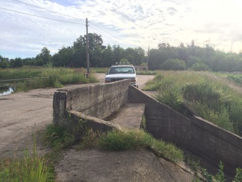 1993 Ford Bronco - A white 1993 Ford Bronco with a light bar on its roof is seen parked on a dirt road next to a concrete barrier.
