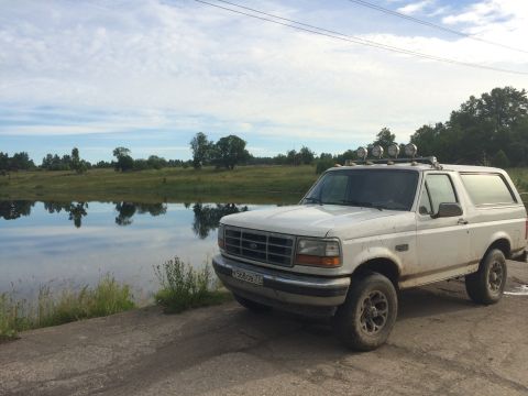 1993 Ford Bronco - A white 1993 Ford Bronco is parked near a body of water under a cloudy sky.