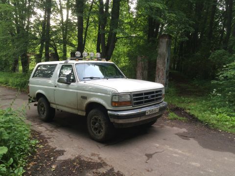 1993 Ford Bronco - This 1993 Ford Bronco is seen parked on a dirt road surrounded by trees, equipped with auxiliary lights on its roof.