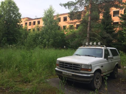 1993 Ford Bronco - White Ford Bronco SUV parked in front of an abandoned building with overgrown vegetation.