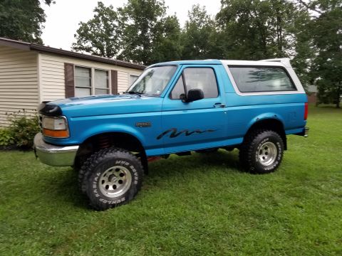 1995 Ford Bronco - A lifted blue Ford Bronco sits on a grassy lawn next to a house.
