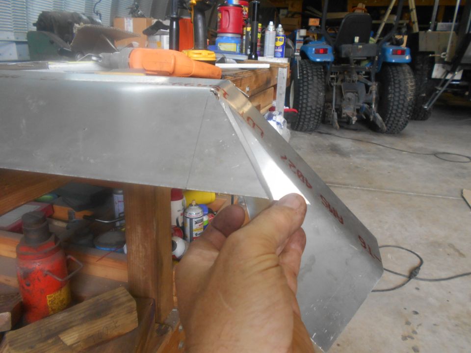 Hand shaping aluminum panel with red markings, tractor in background
