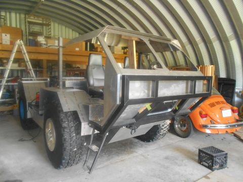1992 Ford Bronco - A partially constructed custom vehicle sits in a workshop next to an orange Volkswagen Beetle.