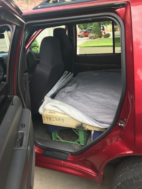 2000 Ford Explorer - The interior of a red 2000 Ford Explorer is set up for camping with a mattress and gear.