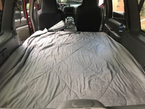2000 Ford Explorer - The rear of an SUV has been converted into a sleeping area with a large, quilted blanket covering the space.