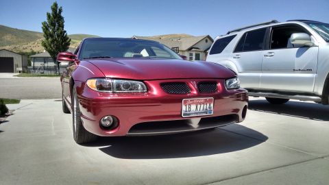 2002 Pontiac Grand Prix - A red 2002 Pontiac Grand Prix is parked in a driveway, with a silver SUV beside it.